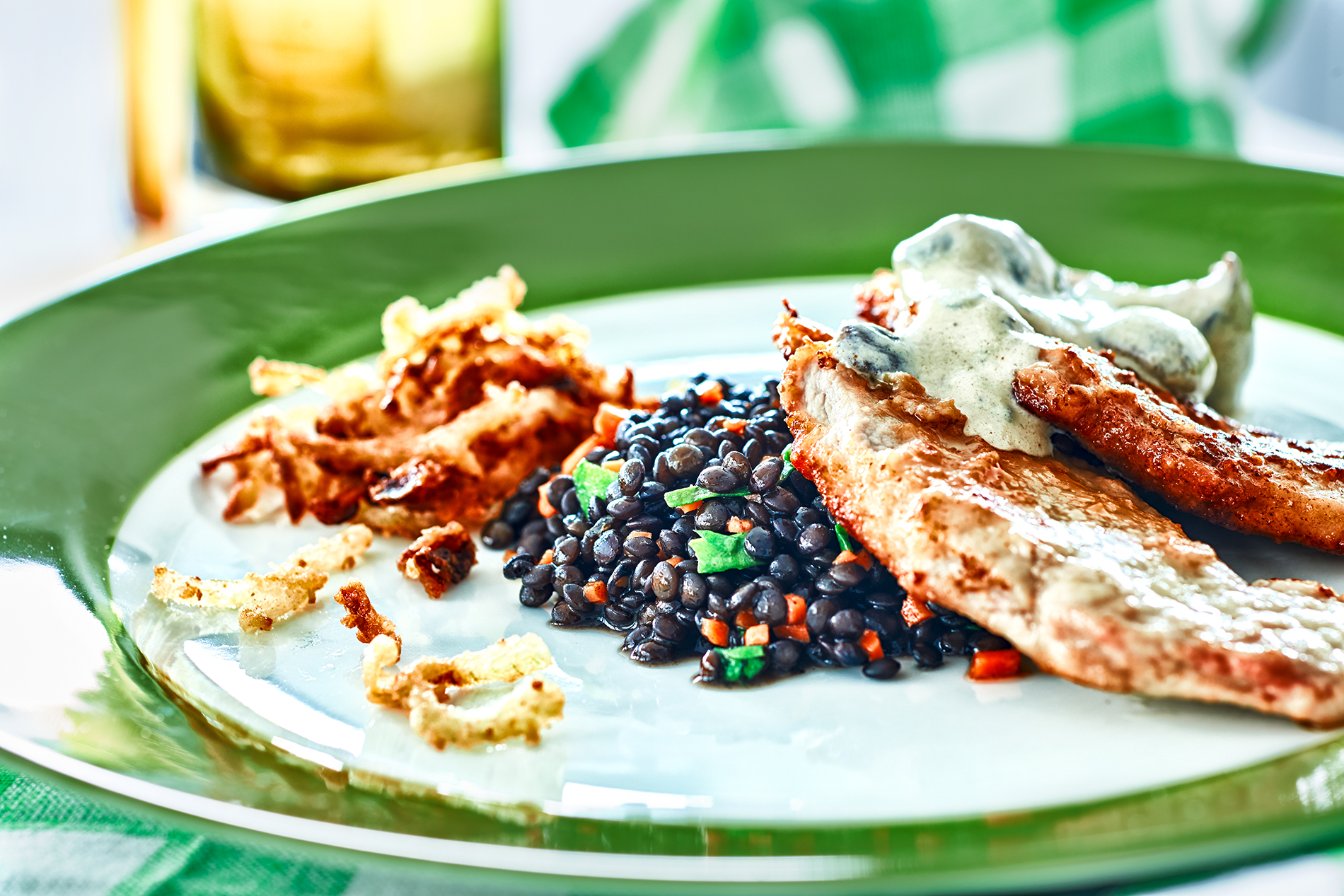 Jägerschnitzel auf einem grün-weißen Teller mit schwarzen Belugalinsen und Kartoffel-Rösti